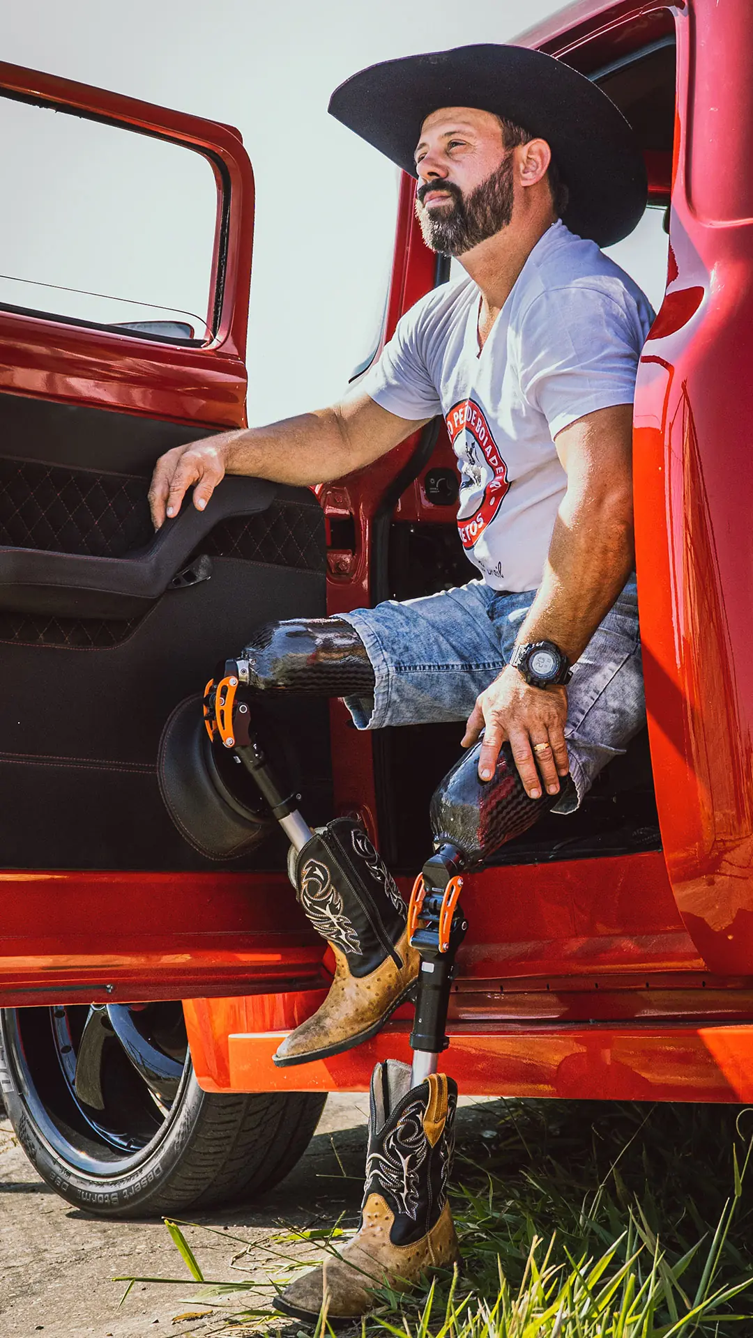 Man in a hat sitting in the door of a red pickup truck, with a leg prosthesis
